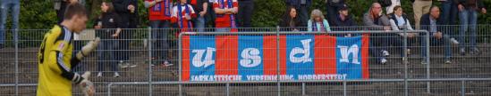 Torhüter in gelbem Trikot vor Tribüne mit Fans und blau-rotem Eintracht-Transpi