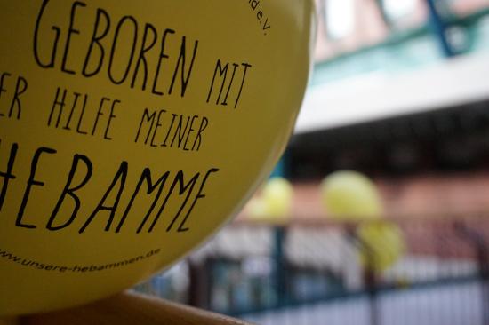 Gelber Luftballon, Aufschrift: Geboren mit der Hilfe einer Hebamme.