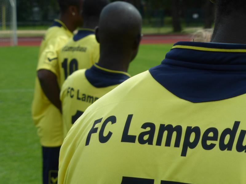 Vier Spieler des FC Lampedusa, gelbe Trikots mit schwarzem Aufdruck von hinten.